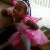 A childhood photo of a little girl in a pink tutu and headband.